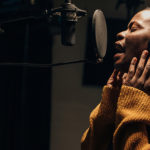 Black female singer singing into microphone in recording studio