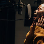 Black female singer singing into microphone in recording studio